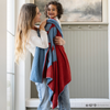 A mother plays with her little boy while holding a receiving blanket with a Superman™ icon on it. The soft blanket is light blue and red. This kids blanket is a luxury blanket and a Saranoni blanket. The blanket is also a double-layer Bamboni® blanket. 