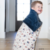 A little boy is wrapped in a soft minky blanket showcasing Superman™ in action, complete with iconic red capes, the Superman™ emblem, comic-style speech bubbles, glasses, and stars. The white background enhances the vibrant red and blue superhero details, while the dark navy plush underside adds extra coziness. Ideal for snuggling, showcasing superhero pride, or adding a fun, adventurous touch to your decor. The soft blanket is a Saranoni blanket. 