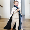 A little boy wrapped in a soft minky blanket showcasing Superman™ in action, complete with iconic red capes, the Superman™ emblem, comic-style speech bubbles, glasses, and stars. The white background enhances the vibrant red and blue superhero details, while the dark navy plush underside adds extra coziness. Ideal for snuggling, showcasing superhero pride, or adding a fun, adventurous touch to your decor. The soft blanket is a Saranoni blanket. 