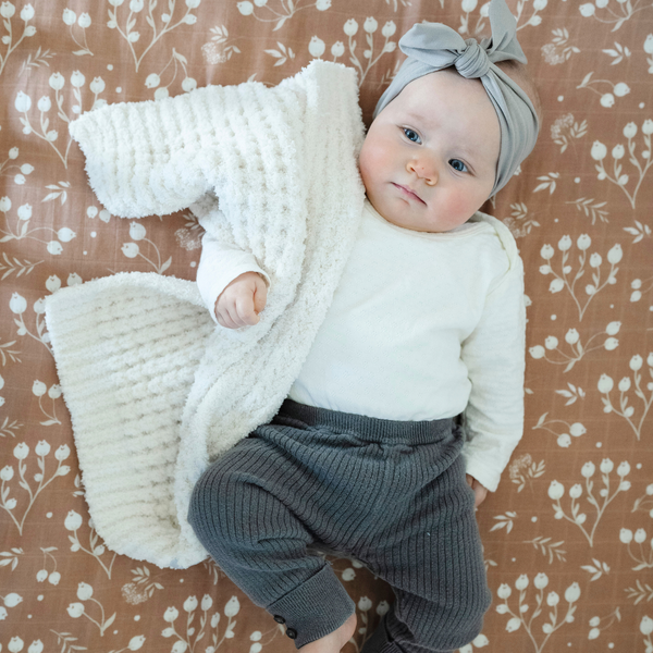 A baby girl holds a buttery-soft Saranoni blanket, featuring a breathable, plush waffle texture in a soothing white hue. This luxury mini blanket is the best baby blanket as a newborn blanket and infant blanket—perfect as a cozy blanket for snuggles or a must-have infant blanket. Designed for softness and comfort, this plush baby blanket makes an ideal baby boy gift or gift for new moms. Enjoy this luxury blanket! 