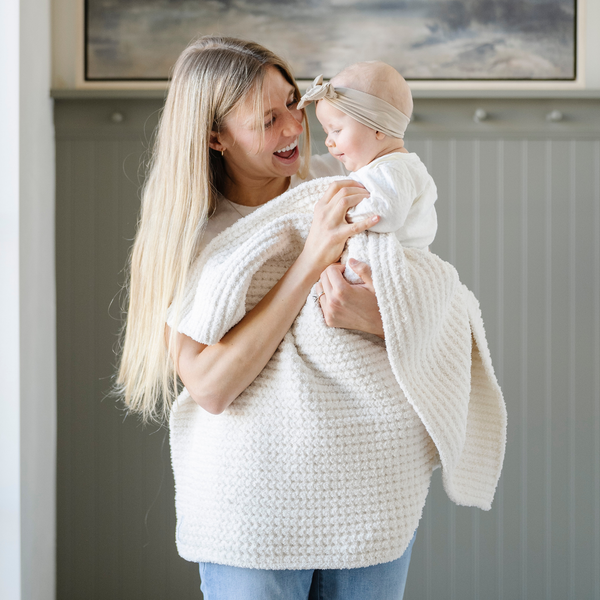 A mother holds her little girl in a buttery-soft Saranoni blanket, featuring a breathable, plush waffle texture in a soothing white hue. This luxury receiving blanket is the best baby blanket as a  newborn blanket, infant blanket, baby blanket, or toddler blanket—perfect as a cozy blanket for snuggles or a must-have infant blanket. Designed for softness and comfort, this plush baby blanket makes an ideal baby gift or gift for new moms. Enjoy this luxury blanket!