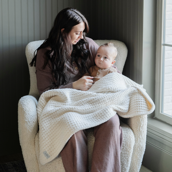 A mother holds her little boy in a buttery-soft Saranoni blanket, featuring a breathable, plush waffle texture in a soothing white hue. This luxury receiving blanket is the best baby blanket as a  newborn blanket, infant blanket, baby blanket, or toddler blanket—perfect as a cozy blanket for snuggles or a must-have infant blanket. Designed for softness and comfort, this plush baby blanket makes an ideal baby gift or gift for new moms. Enjoy this luxury blanket!