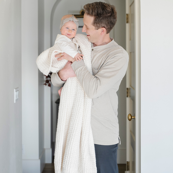 A father holds his little girl in a buttery-soft Saranoni blanket, featuring a breathable, plush waffle texture in a soothing white hue. This luxury receiving blanket is the best baby blanket as a  newborn blanket, infant blanket, baby blanket, or toddler blanket—perfect as a cozy blanket for snuggles or a must-have infant blanket. Designed for softness and comfort, this plush baby blanket makes an ideal baby gift or gift for new moms. Enjoy this luxury blanket!