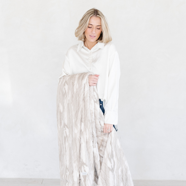 A woman holding a Saranoni blanket, specifically the tan marbled faux fur/minky extra large blanket, highlighting its ultra-soft texture and luxurious design. This plush blanket features a dual-texture blend of silky minky and cozy faux fur, creating the ultimate cozy blanket for home decor. Perfect luxury blanket for lounging or adding style to any space. Soft blanket, cozy blanket—experience unmatched warmth with a Saranoni blanket. 