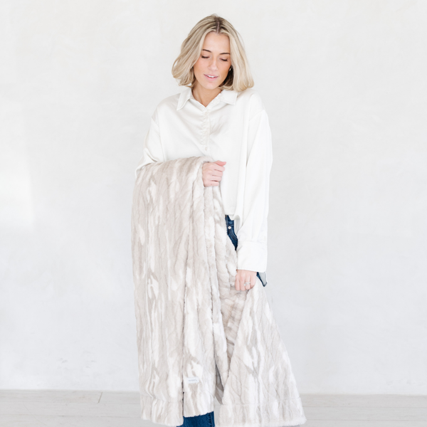 Woman holding a Saranoni blanket, specifically the tan marbled faux fur/minky throw, highlighting its ultra-soft texture and luxurious design. This plush throw blanket features a dual-texture blend of silky minky and cozy faux fur, creating the ultimate cozy throw blanket for home decor. Perfect luxury blanket for lounging or adding style to any space. Soft blanket, cozy blanket, plush throw—experience unmatched warmth with a Saranoni throw blanket.