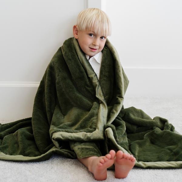 A little boy wrapped in a Toddler Fern Colored Lush Luxury Saranoni Blanket. The soft blanket is a baby blanket or toddler blanket.