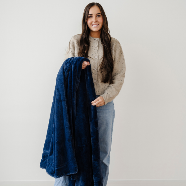 A woman smiles and holds a deep blue blanket that is a lush blanket. This soft blanket is a luxury blanket and a Saranoni blanket. This extra large blanket is great for gifting, relaxing, or as a home decor item. Enjoy this cozy blanket for years to come. 
