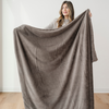 A woman holds up a brown blanket that is a lush blanket and also a Saranoni blanket. This cozy blanket is great for gifting, relaxing, or as a home decor item. This soft blanket is a luxury blanket and an extra large blanket. Enjoy this faux fur blanket for years to come. 