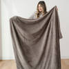 A woman holds up a brown blanket that is a lush blanket. This Saranoni blanket is a soft blanket and a luxury blanket. Use this cozy blanket for gifting, relaxing, or as a home decor staple. This blanket is also an extra large blanket. 