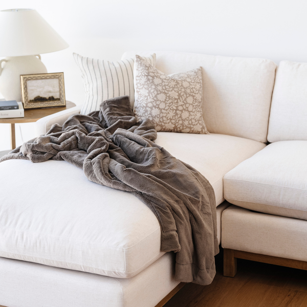 A brown lush blanket that is a Saranoni blanket is beautifully draped on a couch. This soft blanket is a luxury blanket and a faux fur blanket. Use this cozy blanket for gifting, relaxing, or as a home decor staple. Enjoy this extra large blanket for years to come. 