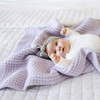 A baby girl with a buttery-soft Saranoni blanket, featuring a breathable, plush waffle texture in a soothing light purple hue. This luxury receiving blanket is the best baby blanket as a  newborn blanket, infant blanket, baby blanket, or toddler blanket—perfect as a cozy blanket for snuggles or a must-have infant blanket. Designed for softness and comfort, this plush baby blanket makes an ideal baby gift or gift for new moms. Enjoy this luxury blanket!