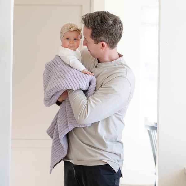 A father holds his little girl in a buttery-soft Saranoni blanket, featuring a breathable, plush waffle texture in a soothing light purple hue. This luxury receiving blanket is the best baby blanket as a  newborn blanket, infant blanket, baby blanket, or toddler blanket—perfect as a cozy blanket for snuggles or a must-have infant blanket. Designed for softness and comfort, this plush baby blanket makes an ideal baby gift or gift for new moms. Enjoy this luxury blanket!