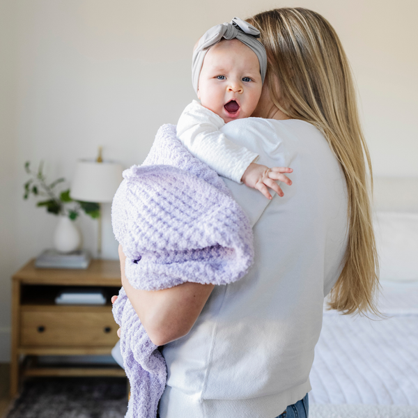 A mother holds her little girl in a buttery-soft Saranoni blanket, featuring a breathable, plush waffle texture in a soothing light purple hue. This luxury receiving blanket is the best baby blanket as a  newborn blanket, infant blanket, baby blanket, or toddler blanket—perfect as a cozy blanket for snuggles or a must-have infant blanket. Designed for softness and comfort, this plush baby blanket makes an ideal baby gift or gift for new moms. Enjoy this luxury blanket!