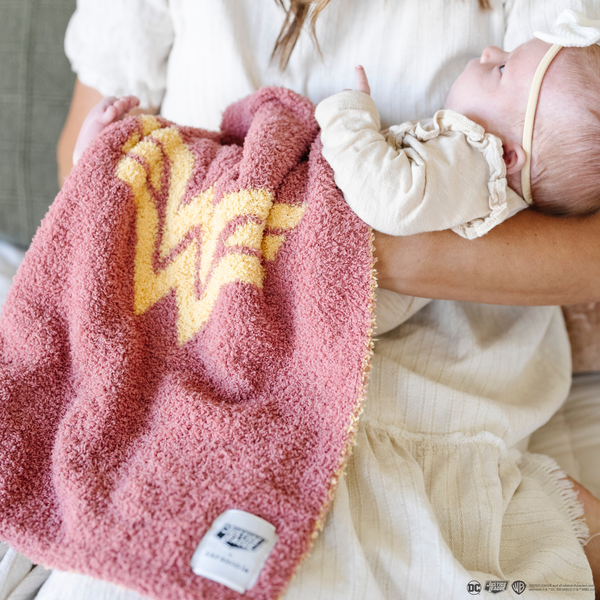 A mother holds her little girl in a pink and yellow double-layer Bamboni® blanket with a Wonder Woman™ icon on it. The soft blanket is a luxury blanket and a mini blanket as well as a Saranoni blanket. This kids blanket is perfect for littles. 