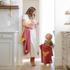 A mother holds her baby girl in a pink and yellow double-layer Bamboni® receiving blanket with a Wonder Woman™ icon on it while standing by her other daughter who is holding the same blanket is a mini size. The soft blankets are luxury blankets and Saranoni blankets. These kids blankets are perfect for littles. 