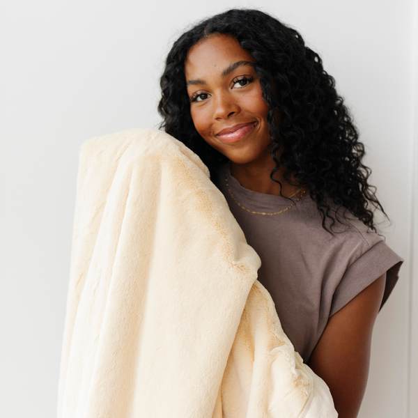 A woman holds a Luxury Extra Large Oversized Throw Chiffon (light yellow) Colored Lush Saranoni Blanket. The soft blanket is an extra large throw blanket and has a soft faux fur feeling.