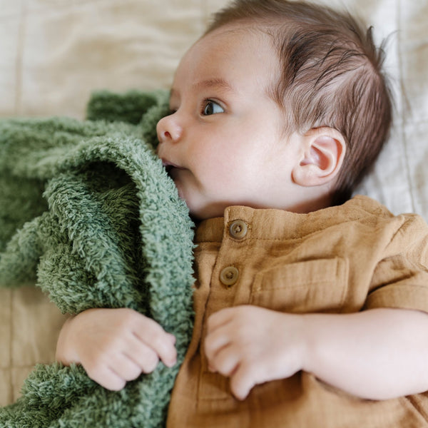 A little boy lays with a lighter green colored Bamboni® Saranoni Blanket. The soft blanket is a small blanket and a baby blanket as well as a mini blanket.