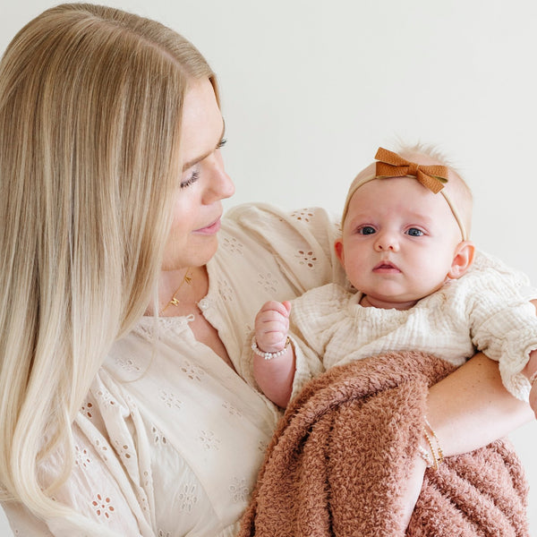 A mother holds her little girl in a French Rose colored Bamboni® Saranoni Blanket. The soft blanket is a small blanket and a baby blanket as well as a mini blanket.