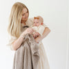 A mother holds her little girl in a taupe colored Bamboni® Saranoni Blanket. The soft blanket is a small blanket and a baby blanket as well as a receiving blanket.