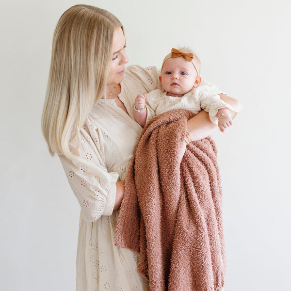 A mother holds her little girl in a French Rose colored Bamboni® Saranoni Blanket. The soft blanket is a small blanket and a baby blanket as well as a receiving blanket.