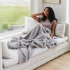 Girl snuggling up on couch by open window with her Gray BAMBONI® XL BLANKETS - Saranoni