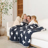 Three little girls sit with a luxurious double-layer Bamboni® blanket by Saranoni, featuring a charcoal and white blanket with a swiss cross pattern. This ultra-soft blanket is crafted from bamboo rayon and poly microfiber, making it lightweight, breathable, and fluffy. Ideal as a cozy throw blanket, luxury blanket, plush throw, soft blanket, or stylish home accent, this Saranoni blanket brings warmth, comfort, and timeless elegance to any living room or bedroom.