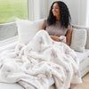 Woman snuggled on the couch with extra soft and stretchy, thick Gray and White HOPE DOUBLE - LAYER BAMBONI® THROW BLANKETS - Saranoni