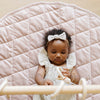 A little girl lays on a soft cameo colored minky play mat in a circle shape, 36 inches in diameter, with durable quilting. Ideal as a portable and quilted baby play mat for on-the-go comfort and easy packing in a diaper bag.