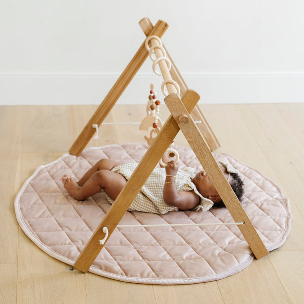 A little girl lays on a soft cameo colored minky play mat in a circle shape, 36 inches in diameter, with durable quilting. Ideal as a portable and quilted baby play mat for on-the-go comfort and easy packing in a diaper bag.