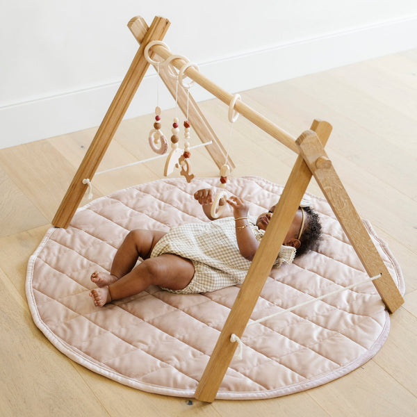 A little girl lays on a soft cameo colored minky play mat in a circle shape, 36 inches in diameter, with durable quilting. Ideal as a portable and quilted baby play mat for on-the-go comfort and easy packing in a diaper bag.