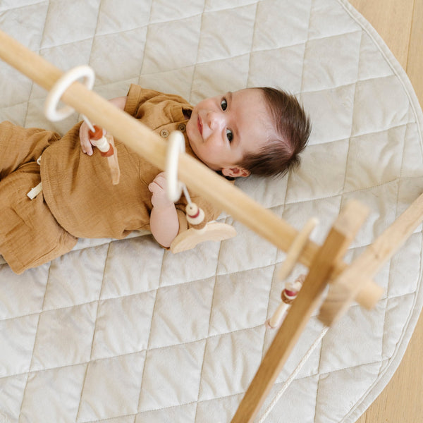 A little boy lays on a soft moonbeam colored minky play mat in a circle shape, 36 inches in diameter, with durable quilting. Ideal as a portable and quilted baby play mat for on-the-go comfort and easy packing in a diaper bag.