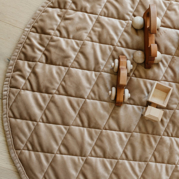 Toys on a soft hazelnut colored minky play mat in a circle shape, 36 inches in diameter, with durable quilting. Ideal as a portable and quilted baby play mat for on-the-go comfort and easy packing in a diaper bag.