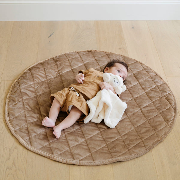 A little boy lays on a soft hazelnut colored minky play mat in a circle shape, 36 inches in diameter, with durable quilting. Ideal as a portable and quilted baby play mat for on-the-go comfort and easy packing in a diaper bag.