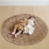 A little boy lays on a soft hazelnut colored minky play mat in a circle shape, 36 inches in diameter, with durable quilting. Ideal as a portable and quilted baby play mat for on-the-go comfort and easy packing in a diaper bag.