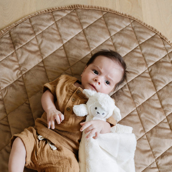 A little boy lays on a soft hazelnut colored minky play mat in a circle shape, 36 inches in diameter, with durable quilting. Ideal as a portable and quilted baby play mat for on-the-go comfort and easy packing in a diaper bag.