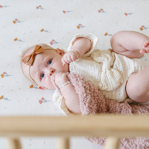 A baby girl lays on a Minky Stretch Luxe crib sheet in a floral pattern, designed with soft and stretchy minky fabric for ultimate comfort. Perfect fit for standard crib mattresses, offering a cozy and luxurious sleep environment for your baby.