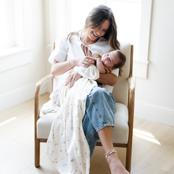 A mother holds her baby boy in a Minky Stretch Luxe swaddle in a mushroom pattern, featuring ultra-soft minky fabric with a luxurious stretch, perfect for keeping your baby cozy and comfortable. Ideal for newborns and infants.