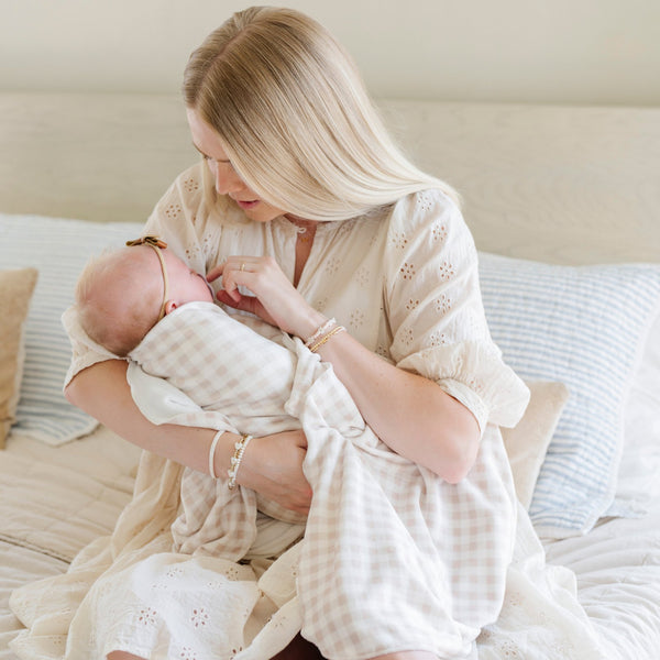 A mother holds her baby girl in a Minky Stretch Luxe swaddle in gingham pattern, featuring ultra-soft minky fabric with a luxurious stretch, perfect for keeping your baby cozy and comfortable. Ideal for newborns and infants.