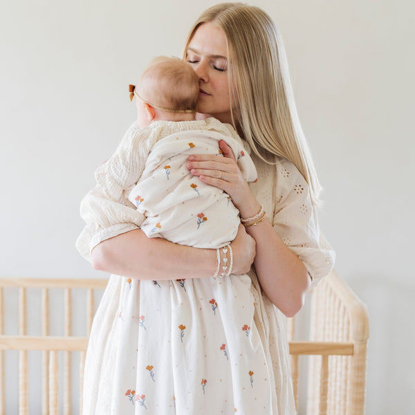 A mother holds her baby girl in a Minky Stretch Luxe swaddle in floral pattern, featuring ultra-soft minky fabric with a luxurious stretch, perfect for keeping your baby cozy and comfortable. Ideal for newborns and infants.