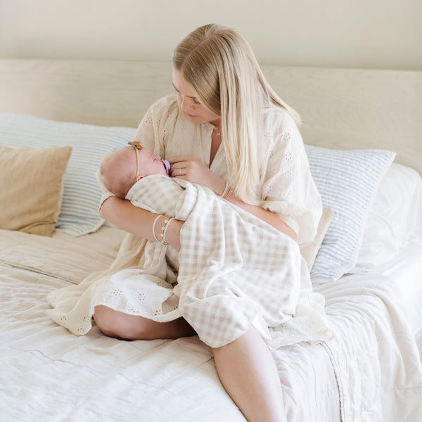 A mother holds her baby girl in a Minky Stretch Luxe swaddle in gingham pattern, featuring ultra-soft minky fabric with a luxurious stretch, perfect for keeping your baby cozy and comfortable. Ideal for newborns and infants.