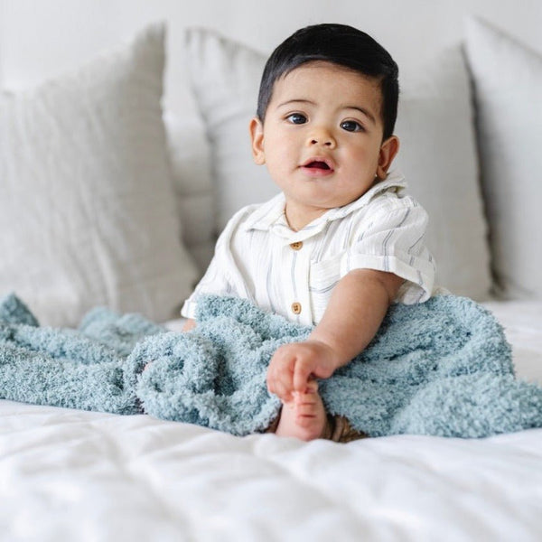 Adorable baby boy sitting on bed, wrapped in Light Blue Surf RIBBED BAMBONI® RECEIVING BLANKETS - Saranoni