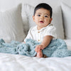 Adorable baby boy sitting on bed, wrapped in Light Blue Surf RIBBED BAMBONI® RECEIVING BLANKETS - Saranoni