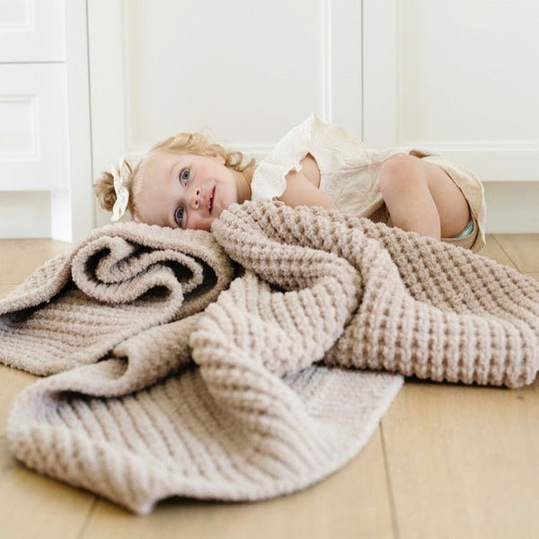 Little girl happily snuggled up with tan waffle knit blanket.