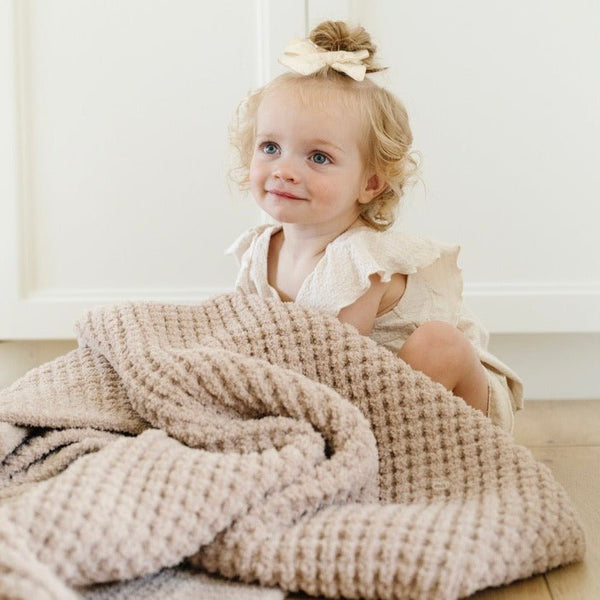 Little girl happily snuggled up with tan waffle knit blanket.