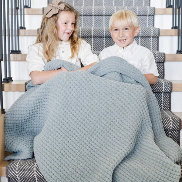 Close-up of siblings cuddling with Elm Waffle Knit Toddler blanket showing its textured pattern