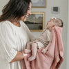 Mom and baby girl bonding together while snuggling with a pink receiving blanket. 