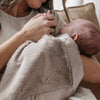 Mom snuggling with baby wrapped in a neutral gray colored satin border blanket. 