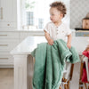 A little boy stands with a Luxury Receiving Seagrass (dusty green) Colored Lush Saranoni Blanket. The soft blanket is a small blanket and a baby blanket or toddler blanket.