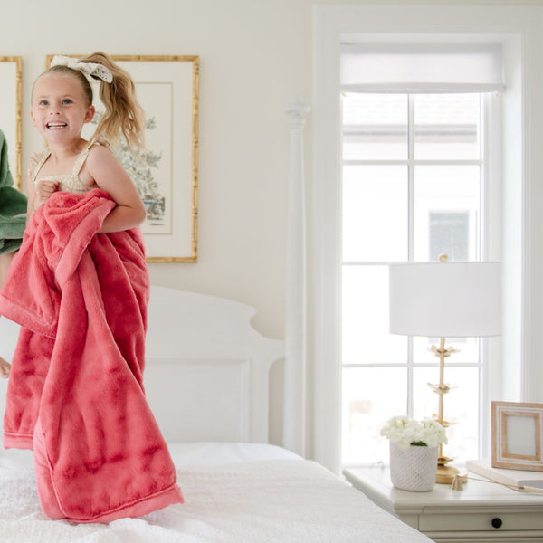 A little girl holds a Toddler Primrose (bold pink) Colored Lush Luxury Saranoni Blanket. The soft blanket is a baby blanket or toddler blanket.