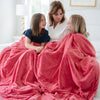 A mother and her two daughters sit under a Luxury Extra Large Oversized Throw Primrose (bold pink) Colored Lush Saranoni Blanket. The soft blanket is an extra large throw blanket and has a soft faux fur feeling.